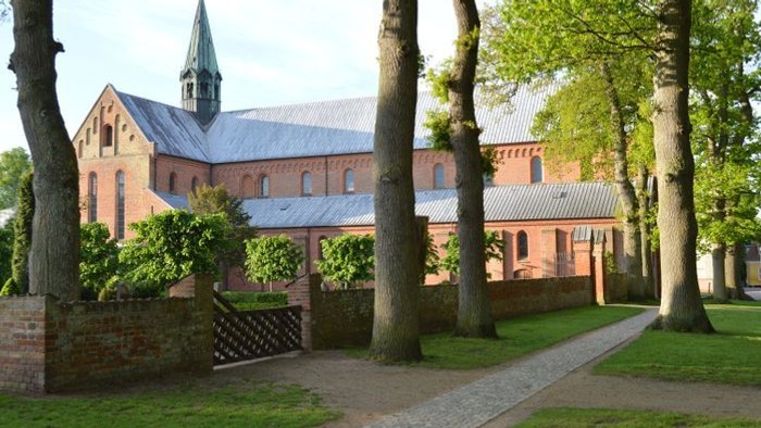 En gammel kirke med spiret og mursten, omgivet af træer og en mur.