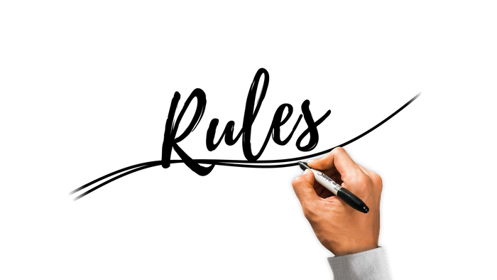 Hand schreibt mit Marker das Wort "Regeln" an eine schwarze Tafel