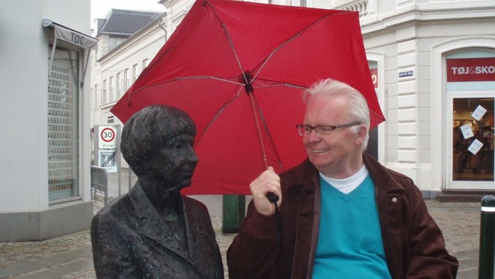 Mand med rød paraply står ved statue.