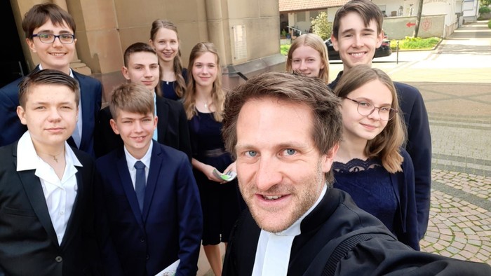 Ein Mann in Anzug mit Gruppe von Jugendlichen vor einem Gebäude