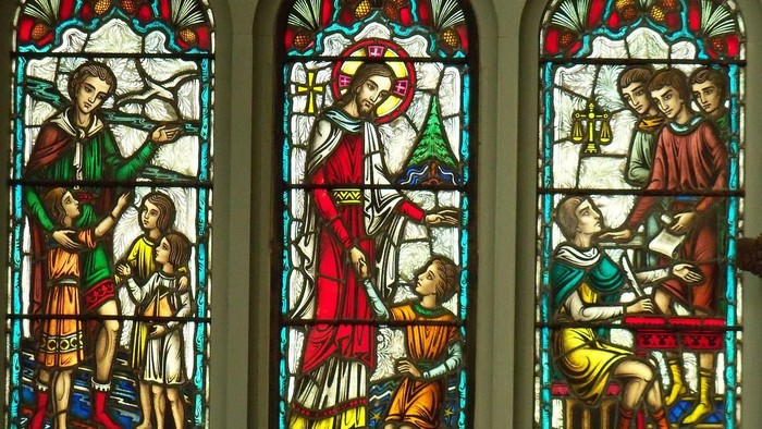 Lebendiges Buntglasfenster mit biblischen Szenen und einer zentralen Figur in rotem Gewand und Heiligenschein.