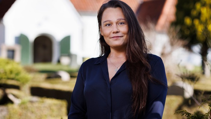 En kvinde står i en have foran et hvidt hus med grønne vinduer.