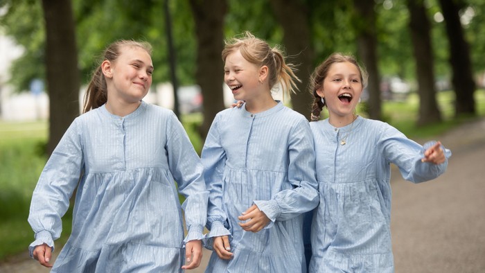 Tre piger i blå kjoler løber og leker i parken