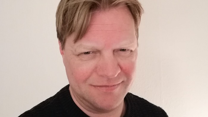 En mand med kort blond hair og en sort trøje.