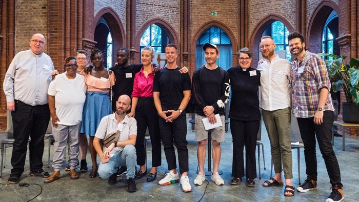 Eine Gruppe von Menschen posiert vor einem Backsteingebäude mit bogenförmigen Fenstern.
