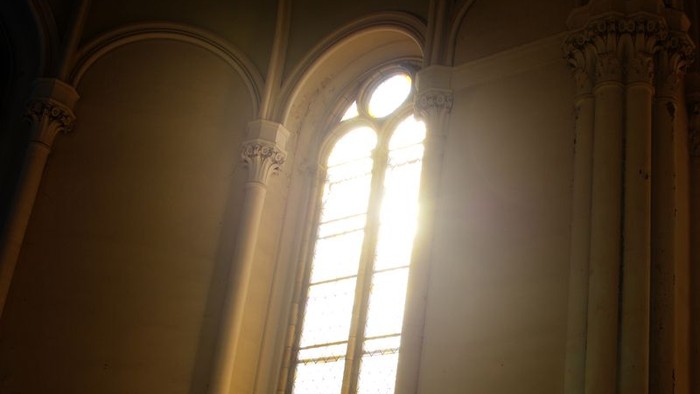 Mann steht vor großem Kirchenfenster im Sonnenlicht