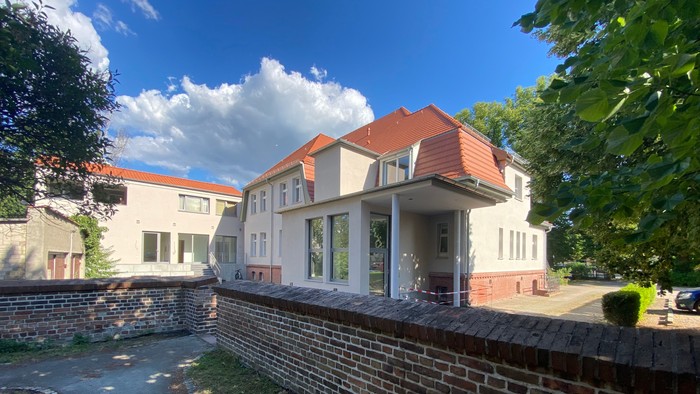 Zwei Häuser mit roten Dächern und weißer Fassade hinter Ziegelmauer