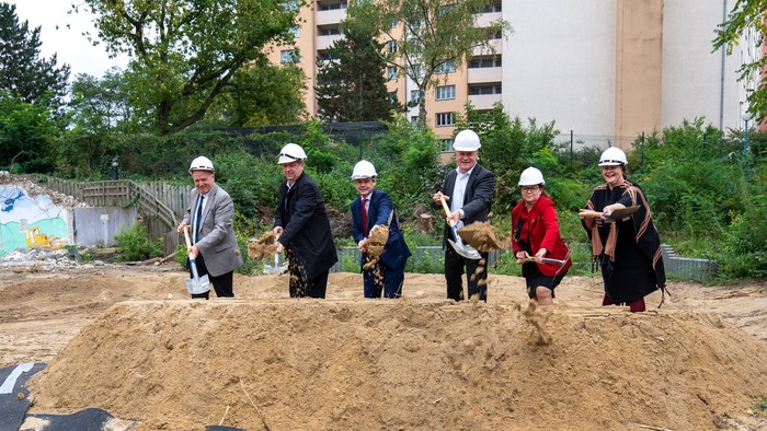Fünf Personen mit Helmen graben bei einem Bauprojekt.
