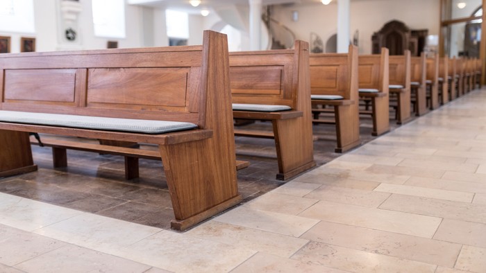 Holzbänke in einer Kirche, mit weißen Sitzflächen, in Reihen angeordnet.