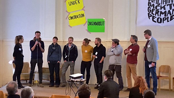 Eine Gruppe von Menschen diskutiert auf einer Bühne vor einem Publikum.