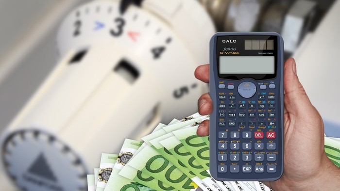 Eine Hand hält einen Taschenrechner über einen Stapel Euro-Scheine mit einer Uhr im Hintergrund.