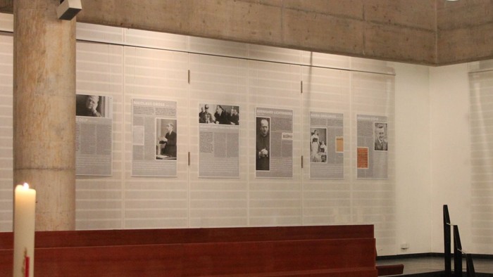 Ein Kircheninneres mit Holzbänken, Kerzen und einer Wand mit Fotos.