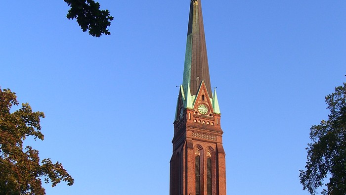 Hohe Kirchturmspitze mit goldener Spitze in klarem Blauhimmel