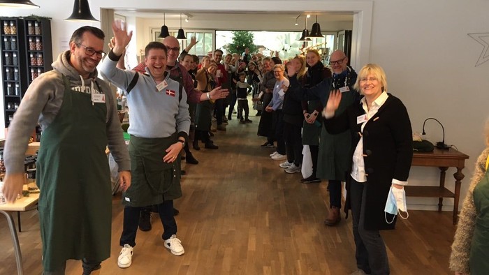 En gruppe mennesker hygger sig i et rum med trægolv og hængelamper.