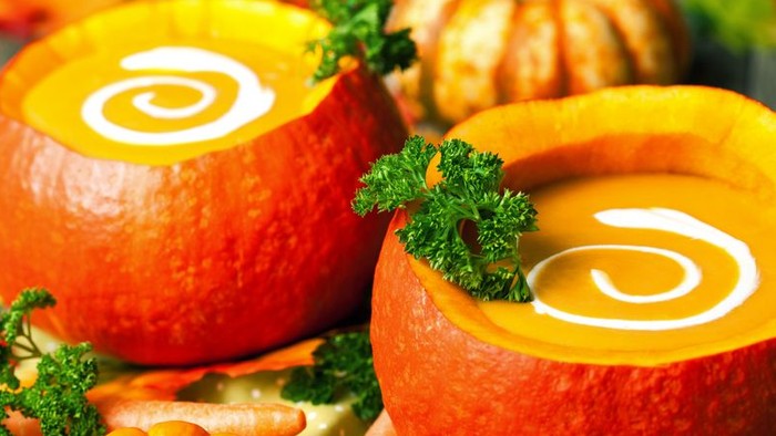 Zwei Kürbisschalen mit Suppe und Petersilie, umgeben von Gemüse