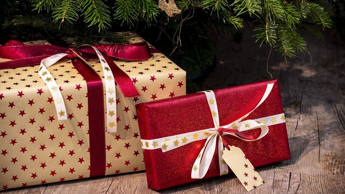 To gaver under juletreet, en med rød og den anden med mørkbrun papir og hvid snurrebånd.