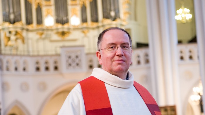 Mann in weiß-roter Soutane vor Kirchenorgel
