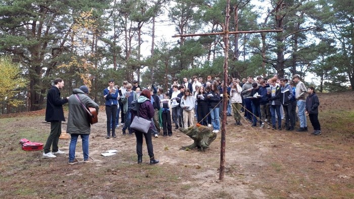 Eine Gruppe von Menschen versammelt sich im Wald um ein Kreuz.