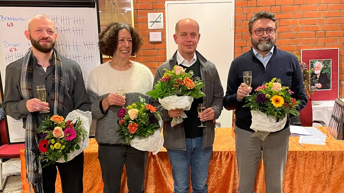 Vier Personen halten Blumensträuße und Gläser und feiern mit fröhlichen Gesichtern ein Ereignis drinnen.