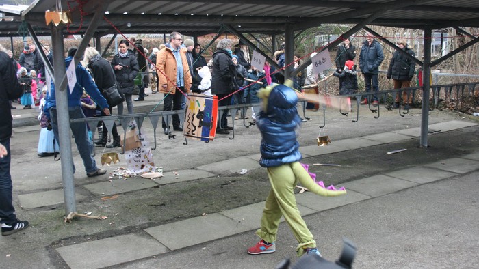 En gruppe mennesker samles under et tagtøj, hvor en person i blå og gule klær danser med en flag.