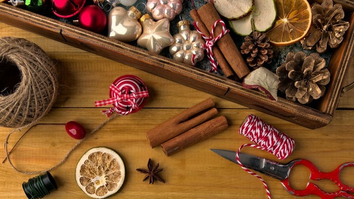 Eine festliche Bastelschale gefüllt mit Weihnachtsdekorationen, Bändern, Zimtstangen und getrockneten Orangen für DIY-Weihnachtsprojekte.