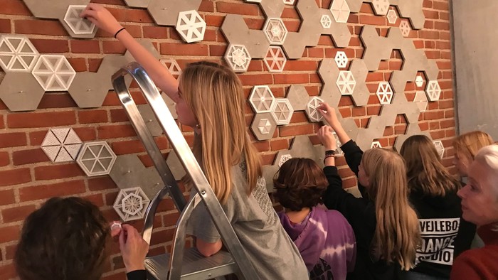 En gruppe af mennesker interagerer med geometriske udsmykninger på en mur.