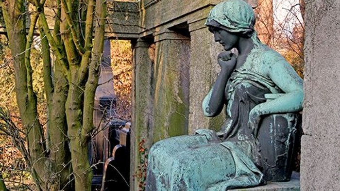 Die Bronzestatue einer Frau sitzt nachdenklich auf einem Sockel.