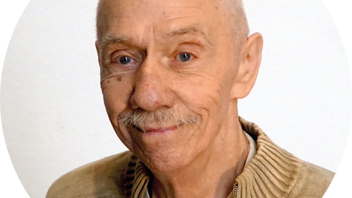 Ein älterer Mann mit Glatze und Schnurrbart lächelt in die Kamera.