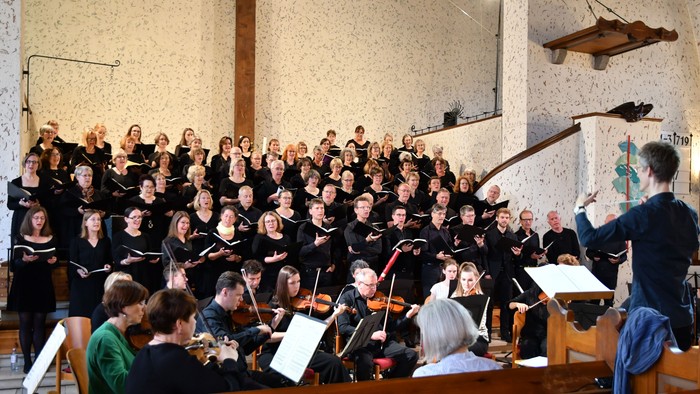 Ein großer Chor singt in einer Kirche, dirigiert von einem Mann im Anzug