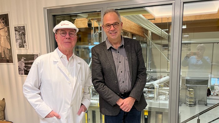 Zwei Männer stehen vor einer Glaswand in einem Labor.