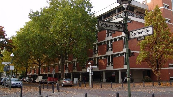 Baumgesäumte Straße mit rotem Backsteingebäude und Straßenschildern