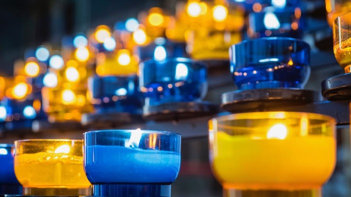 Reihe brennender Kerzen in blauen und gelben Gläsern