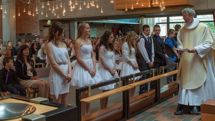 En præst udfører en ceremoni for en gruppe unge piger i hvide kler.