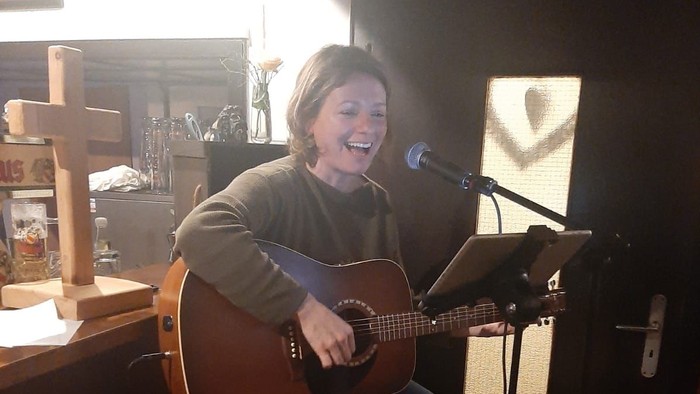 Frau spielt Gitarre und singt in einem Raum