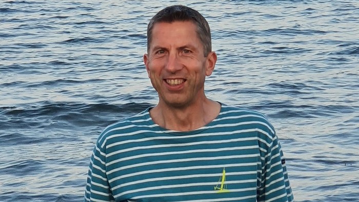 Ein Mann lächelt in die Kamera, während er im Meer steht.