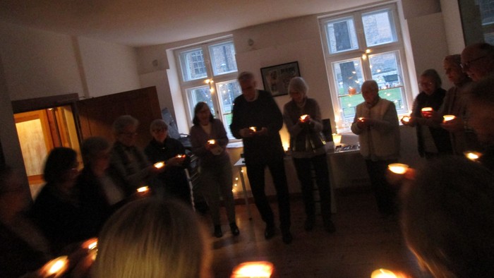 Ein Raum mit Menschen, die Kerzen halten und sich unterhalten.