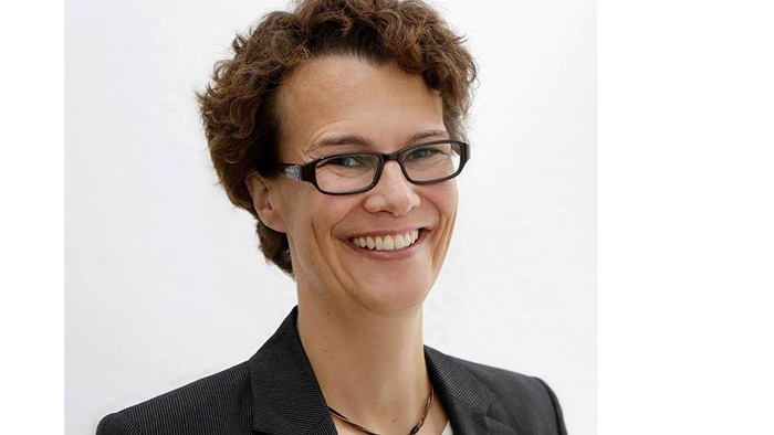 Eine Frau mit kurzem, lockigem Haar und Brille lächelt in die Kamera.