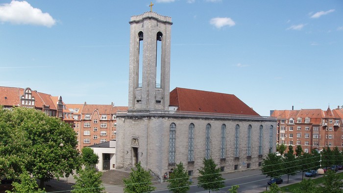 Stor kirke med højt tårn og røde tag i bymiljø