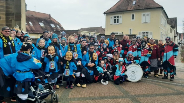 Eine Gruppe von Menschen in blauen und roten Kostümen posiert vor einem Haus