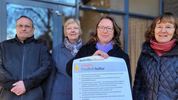 Vier Personen halten ein Informationsblatt zur Friedhofskultur