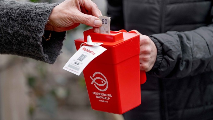 En person kaster penge i en rød samlingskasse.