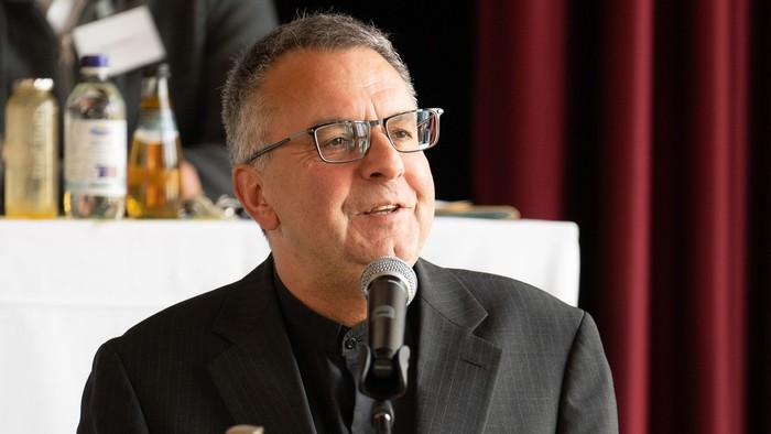 Mann spricht hinter Mikrofon bei Tisch mit Blumenstrauß