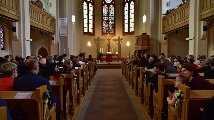 Gottesdienst in einer Kirche, Menschen sitzen in Kirchenbänken, Altarraum mit Kreuz und Kerzen.