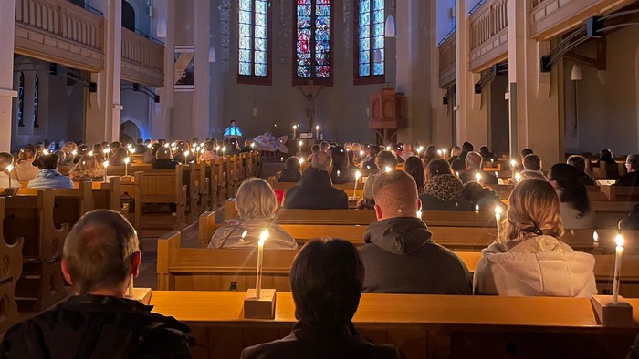 In der Kirche sitzen Menschen in Kirchenbänken, vor ihnen brennen Kerzen.