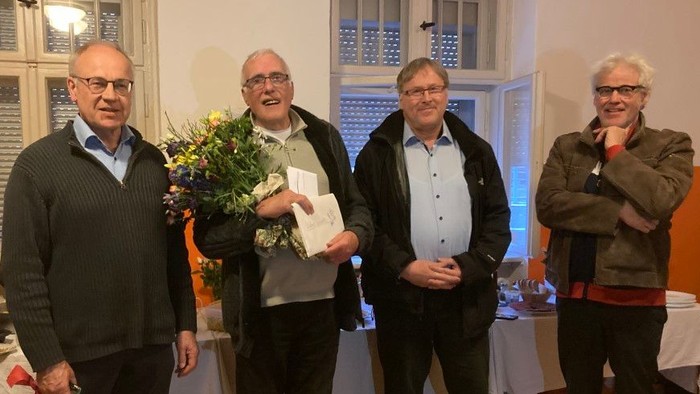 Vier Personen stehen in einem Raum, eine hält Blumen und eine Urkunde.