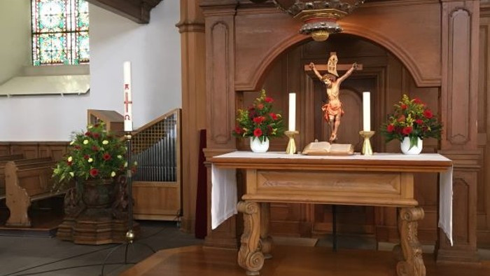 In der Kirche steht ein Altar mit Kruzifix und Blumen.