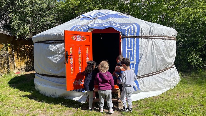Drei Kinder stehen vor einem weißen Zelt mit blauen Mustern im Garten.