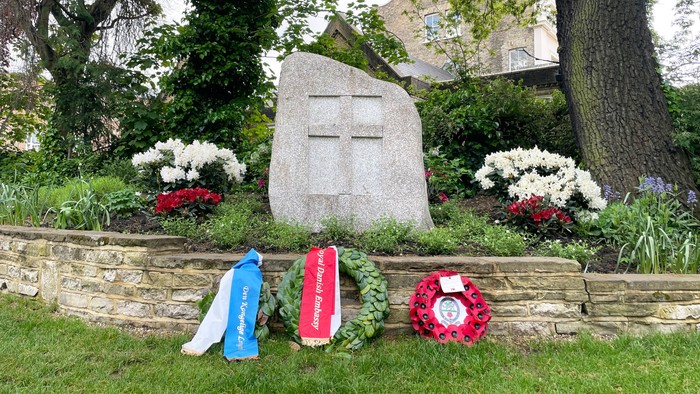 En grav med en stor stenkors og blomsterarrangementer i en trækirkegård