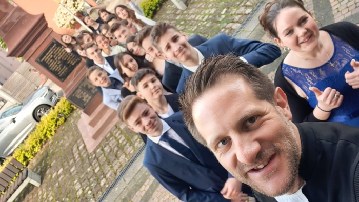 Ein Mann macht ein Selfie mit einer Gruppe von Freunden auf einer Kopfsteinpflasterstraße.