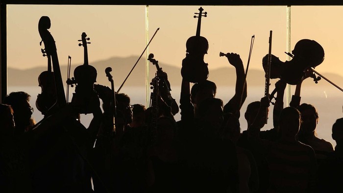 Orchester im Gegenlicht, das vor einem Sonnenuntergangshintergrund Instrumente spielt.
